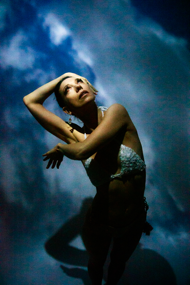 A women in a bikini standing in the sky, with her hands overhead.