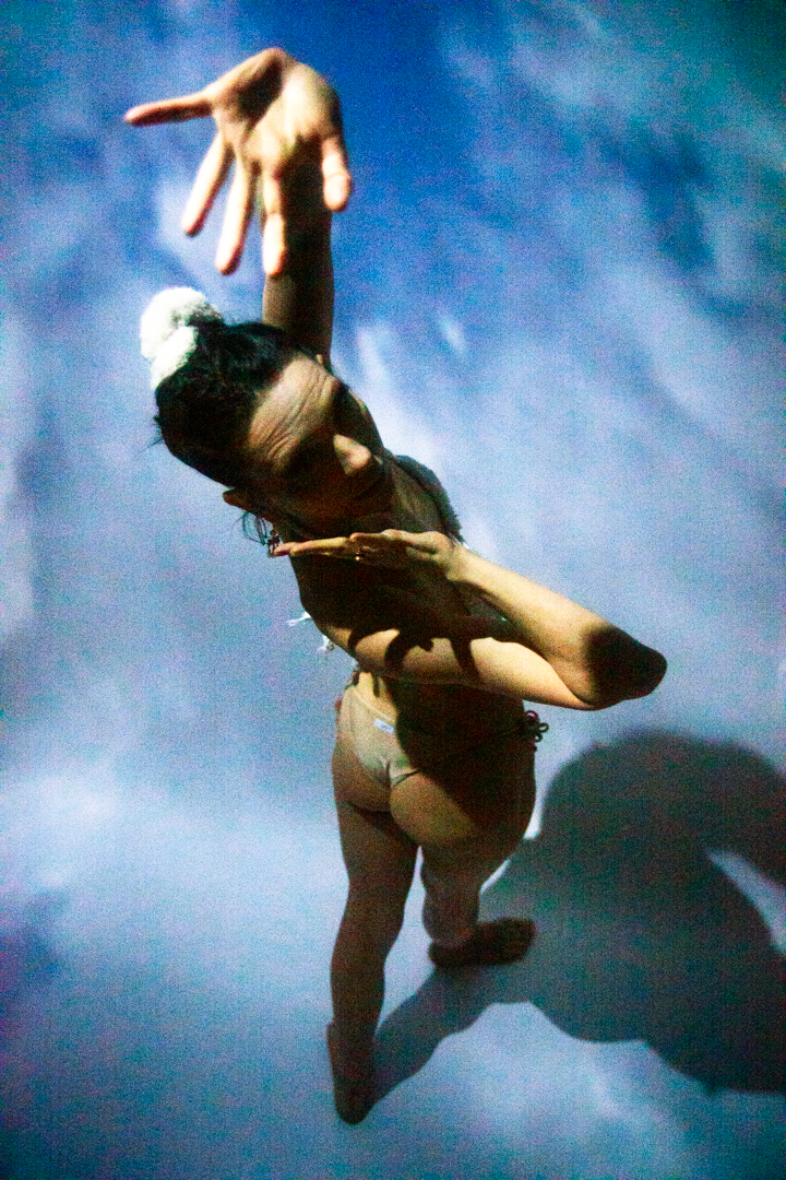 A women in a bikini standing in the sky, with her reaching toward the camera.