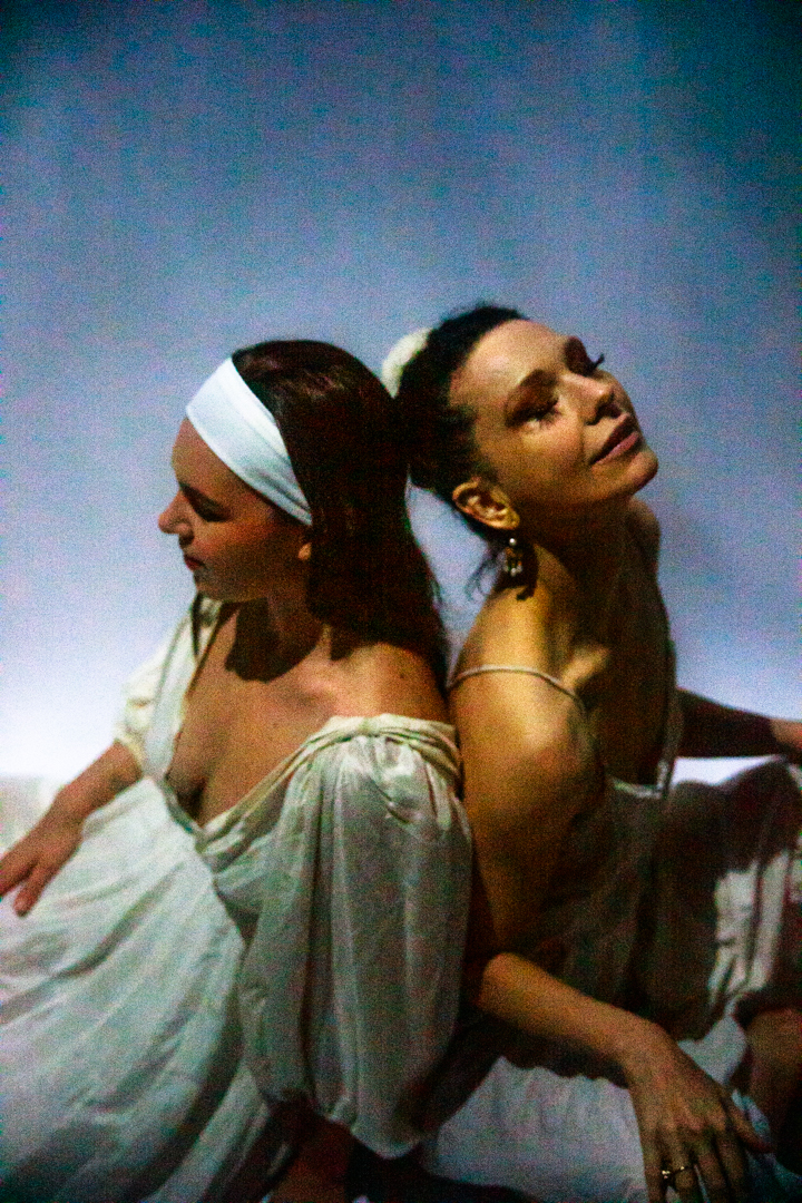 Two women sitting in the sky back to back.